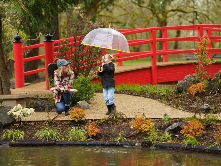 A mother kneels beside her daughter in front of a red bridge.